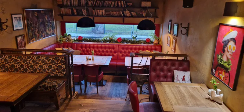 Restorano salė su raudonais minkštasuoliais ir knygų lentyna